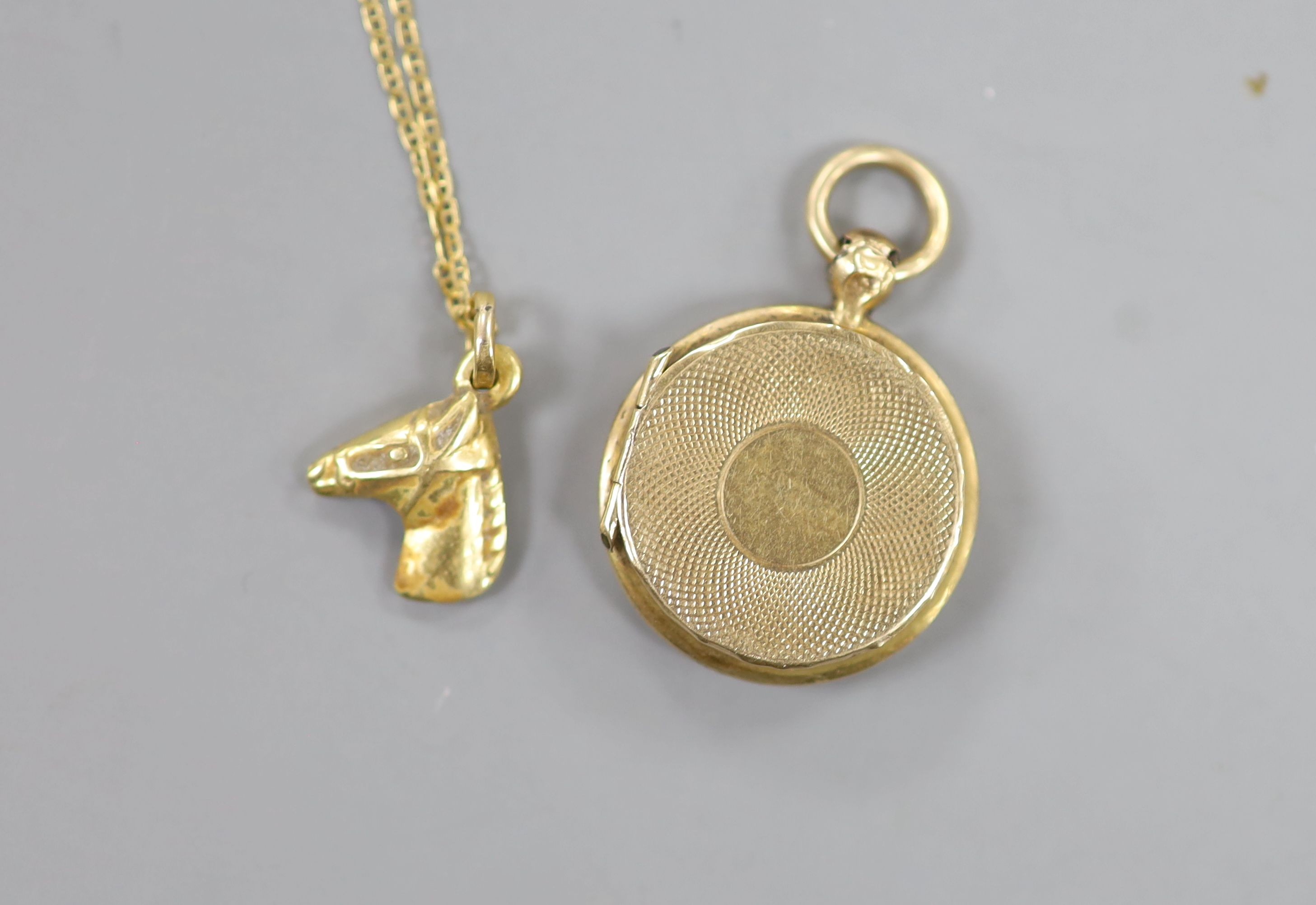 A small early 20th century yellow metal and enamel pendant locket, 18mm, together with a very small horse head pendant on an 18kt fine link chain, gross 5.3 grams.